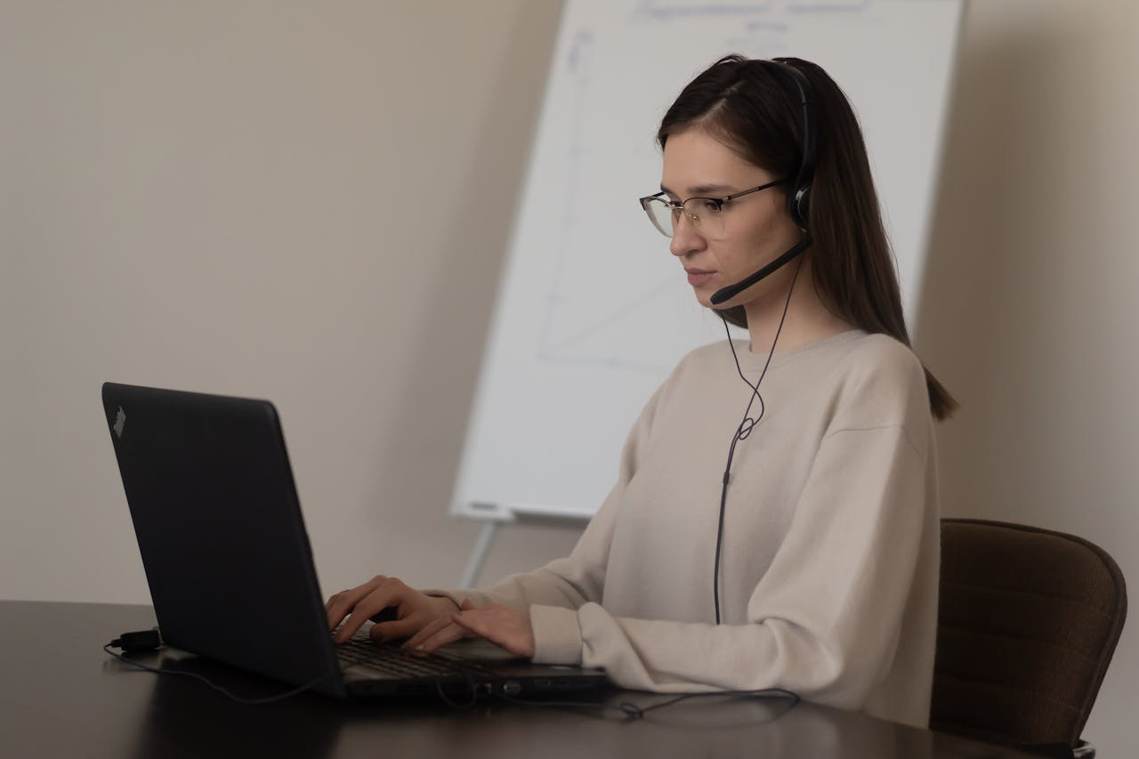 The Art of Drawing Readers In: Your attractive post title goes here Serious young woman in casual outfit with eyeglasses sitting on chair at table and working on laptop with headphones with microphone near whiteboard in bright workplace
