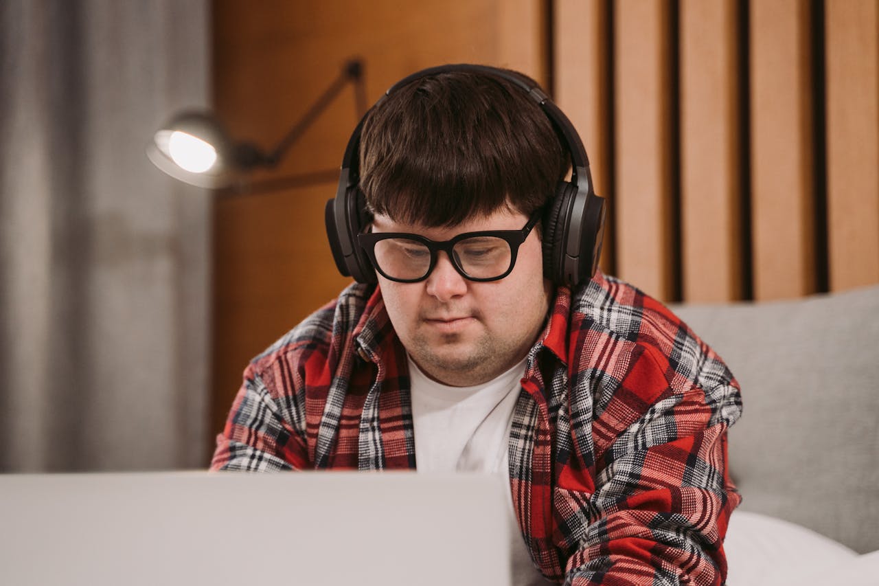 Crafting Captivating Headlines: Your awesome post title goes here Young man wearing headphones and glasses using a laptop indoors. Relaxed and focused setting.